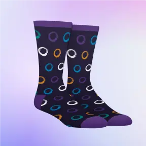 A pair of dark purple crew dress socks displayed against a soft purple gradient background. The socks feature a playful pattern of multicolored rings in white, teal, orange, and blue, with solid purple accents at the toes, heels, and cuffs.